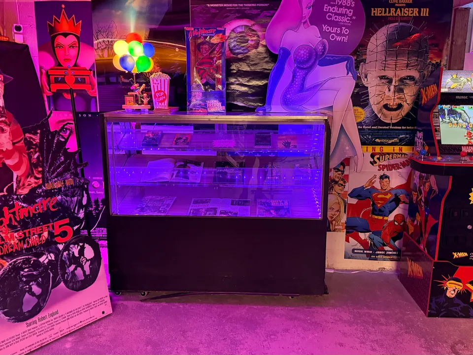 A purple-lit glass display case between movie standees and an X-Men arcade cabinet in the basement.